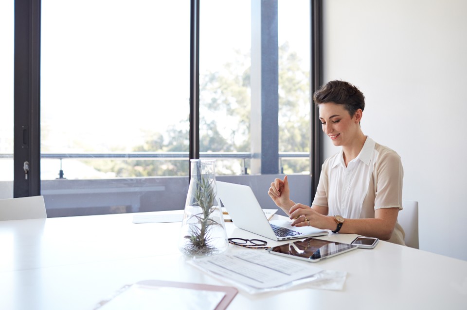 Person smiling looking at laptop, working at large desk in meeting room