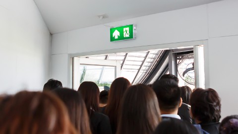 Una multitud de personas saliendo por la puerta de salida de emergencia, demostrando la capacidad de seguimiento de agrupamiento para emergencias.