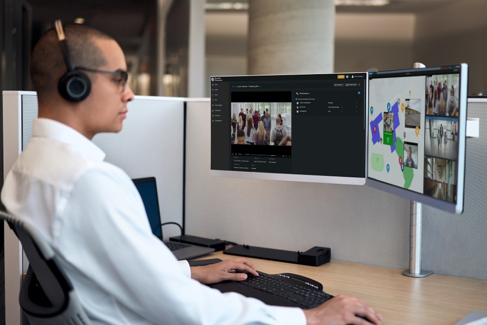 Beveiligingsoperator bewaakt een geünificeerd campusbeveiligingssysteem op twee schermen met behulp van campusvideobewaking en campustoegangscontroledashboards voor volledig overzicht van de campus.