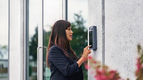 Eine Frau nutzt eine Sprechanlage mit Zugang zu Gebäudezutrittskontrolllösungen. 
