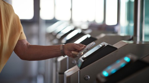 Medewerker die een credential laat zien bij een slimme campustoegangscontrolelezer met een geünificeerd campusbeveiligingssysteem dat het onderhoud vereenvoudigt en het risico op credentials in alle campusfaciliteiten vermindert.